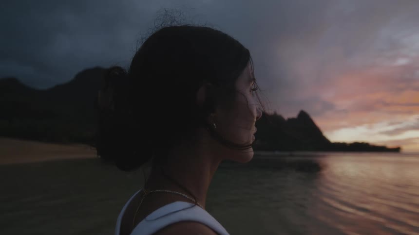 A woman standing at the river bank close to some rocks during sundown