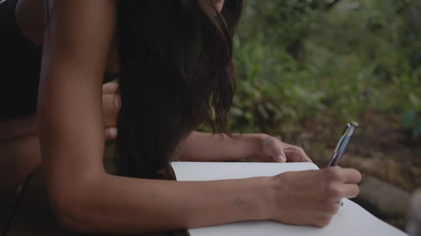 Young woman sitting down on the floor of a porch writing on a notebook during day time