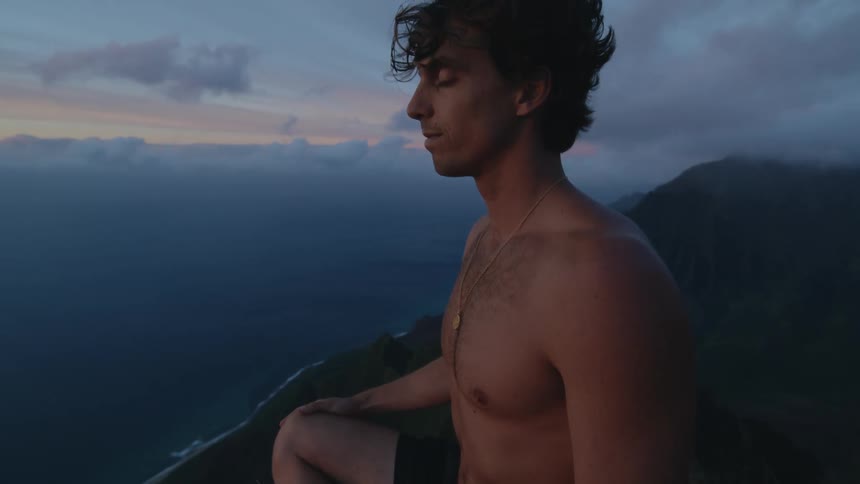 Close up of a man sitting on the edge of a mountain meditating in nature with clouds over the landscape