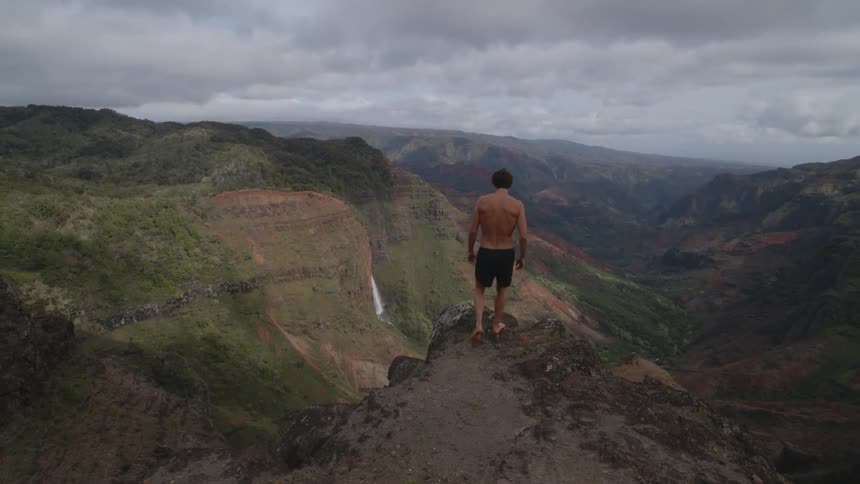 Strong muscular shirtless man walks to the edge of a cliff