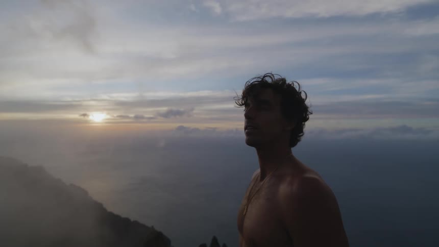 Shirtless man stand on a highland while looking around at sunset
