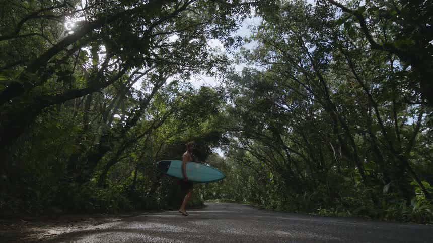 A man is carrying his surfboard on the path in the woods