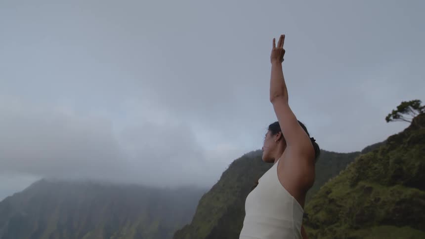 A woman practicing yoga on top of a mountain on a cloudy day