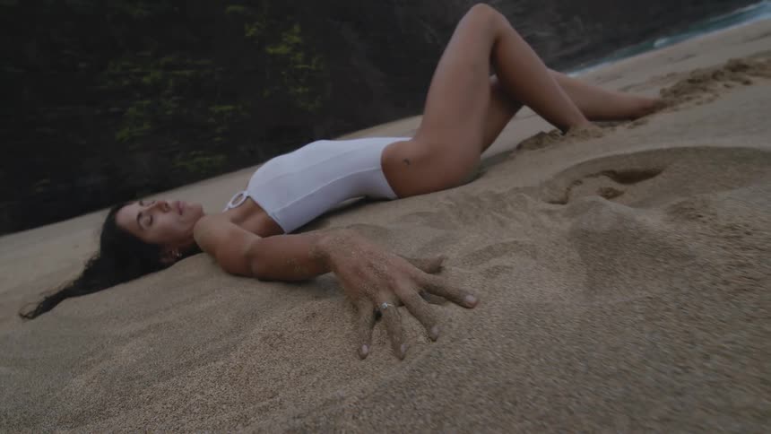 Young woman in a white swimsuit rest on the beach sand next to the ocean