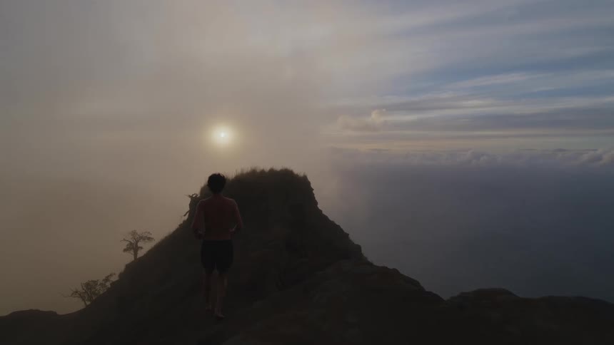 Silhouette of a man running on a mountain overlooking clouds and the sun rising on the horizon