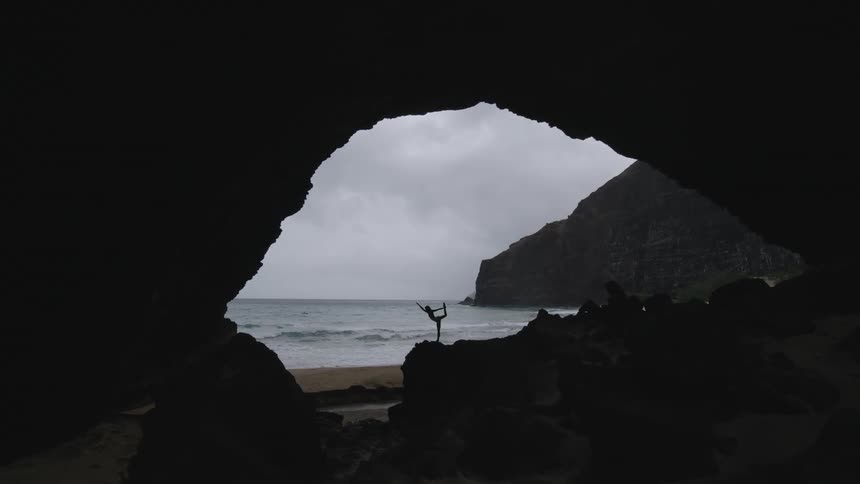 Person does yoga on the beach framed by a cave