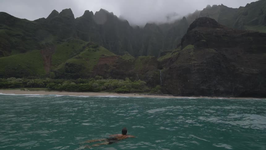 Man floats in the ocean near shore and mountains
