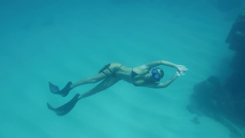 A young woman swimming under the sea with diving goggles and flippers