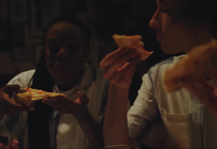 People eating pizza from a table with their hands and talking