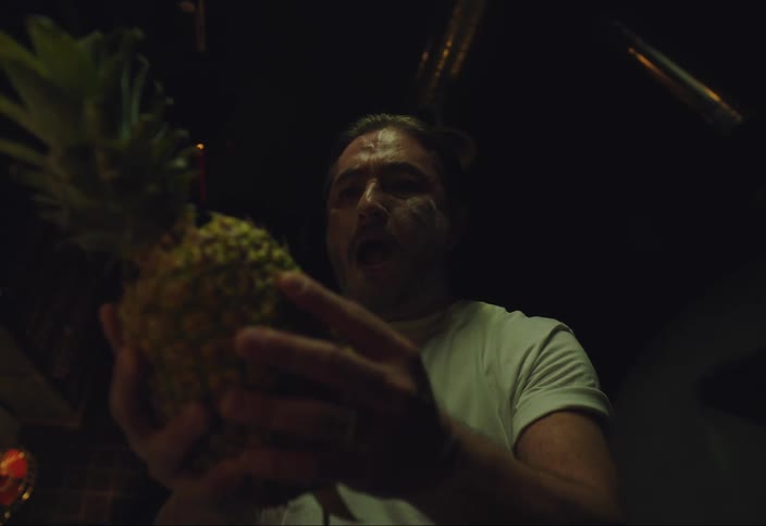 A man takes a pineapple with his hands and soon after makes expressions of nervousness