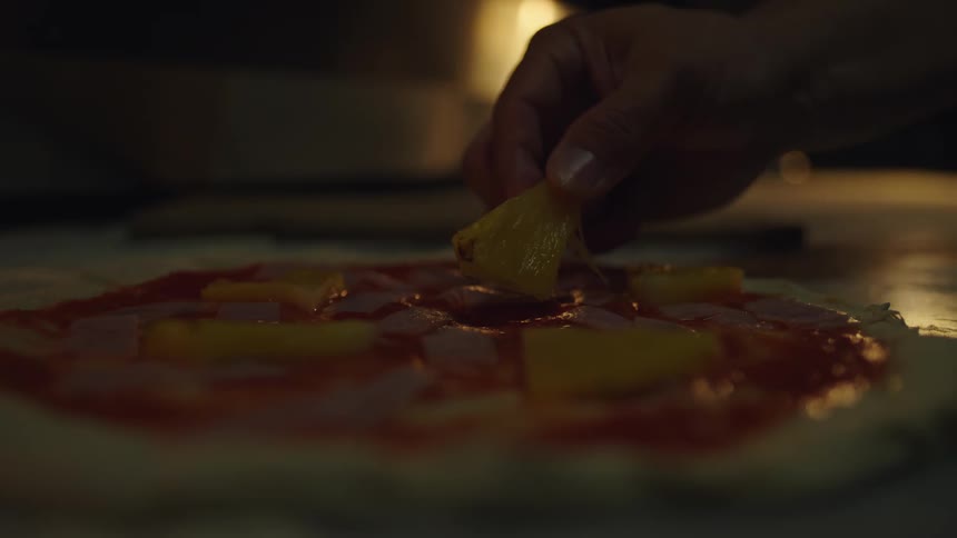Close up of sauce on a pizza as a persons hand puts a pepper on top