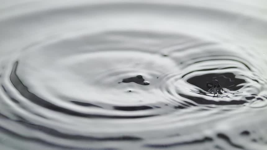 Close up of droplets splashing onto the surface of water creating ripples across the top
