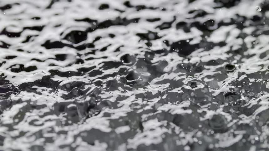 Several water droplets falling into a liquid creating various punctures and ripples