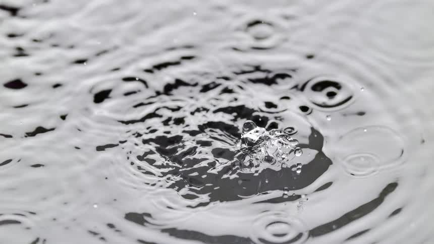 Close up of a slow motion water droplet splashing into water creating rippleson the surface during the day