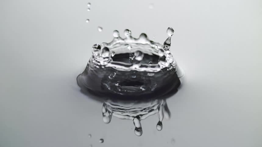 Droplets of water falling onto a liquid surface and creating impact and splashes in slow motion
