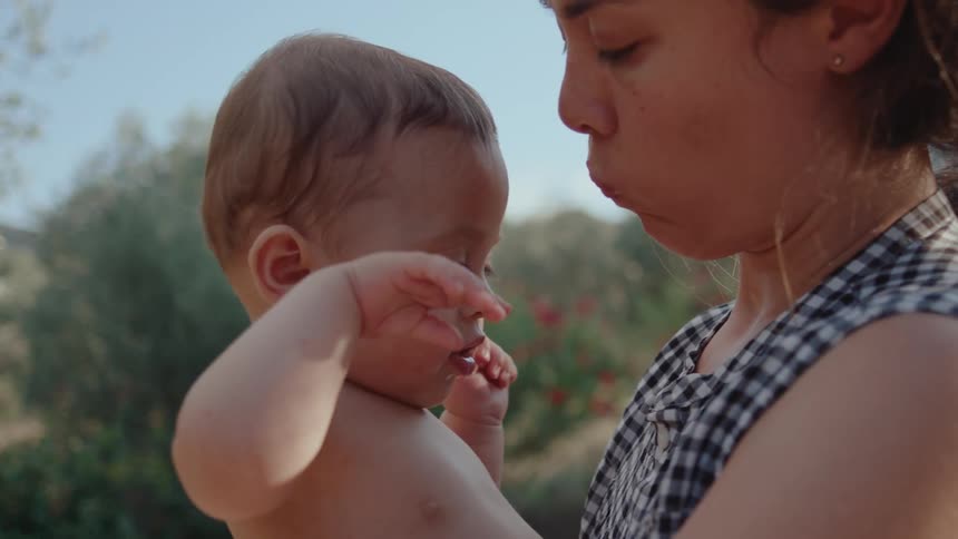 A baby suddenly smiles and lifts arms in air with joy whilst being held by mother