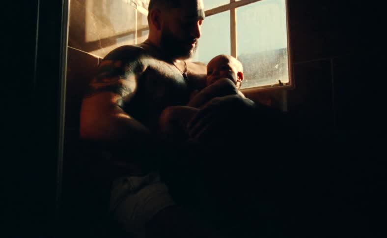 Shirtless father sitting and holding his baby in his arms