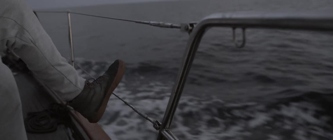 A man's foot is on the railing of a moving ship