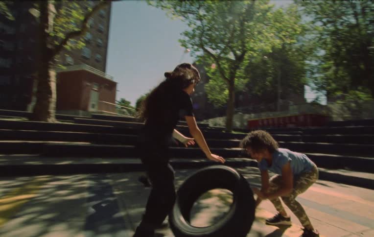 Three children roll a tire and play outdoors near stairs