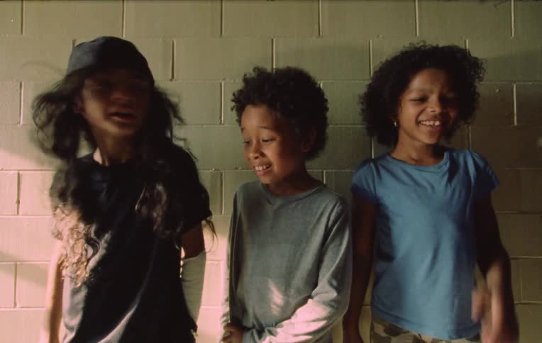 Three children playing and laughing by the white brick wall