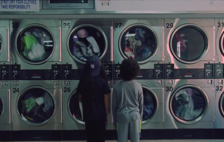 Two children stand inside a laundry mat watching the clothes move in the dryers