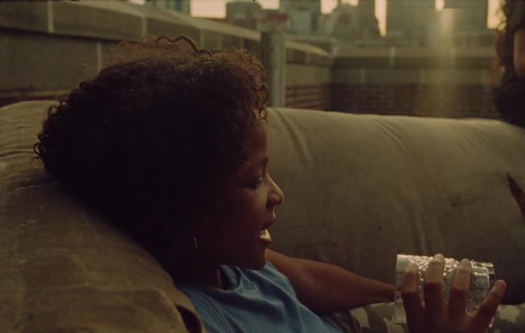 A kid holding a glass cup and laying on the sofa while having a conversation