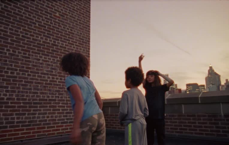 Three children on a building terrace playing and throwing objects against the wall