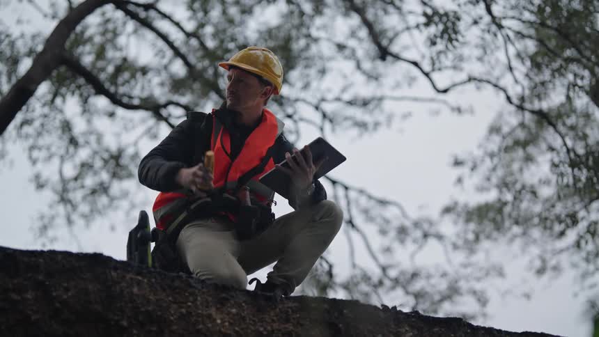A crouching man in safety clothing is holding a tablet in one hand and a flashlight in the other inspecting the surroundings
