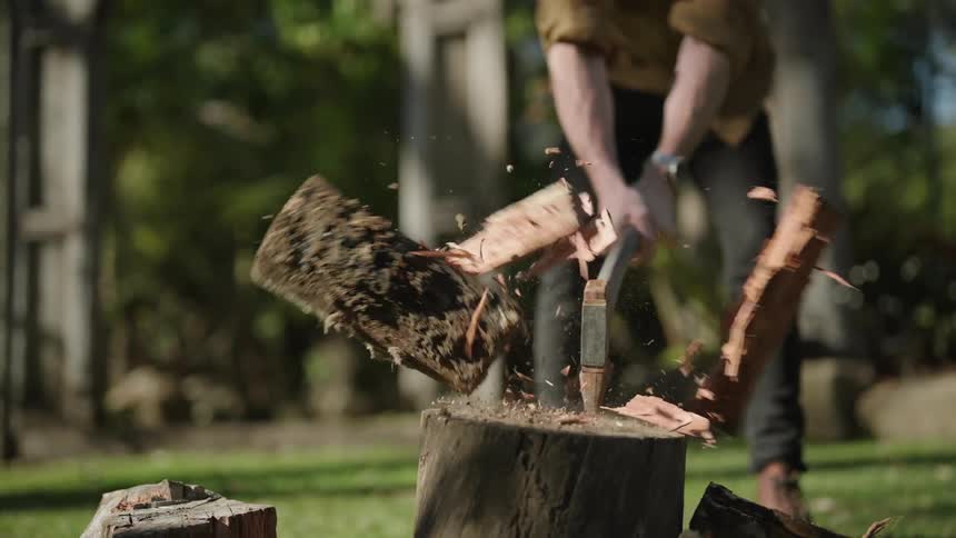 A man delivering an axe to a log and splitting it in half turning it into firewood