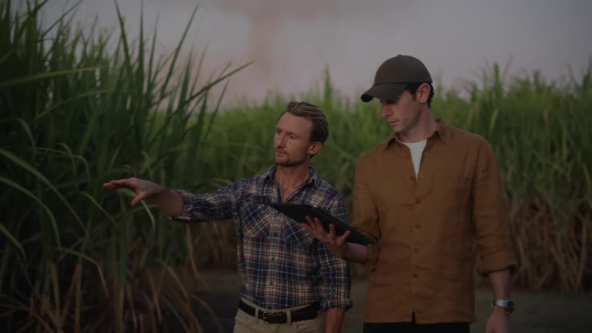Two men walk and talk while pointing to fields of crops and holding a tablet