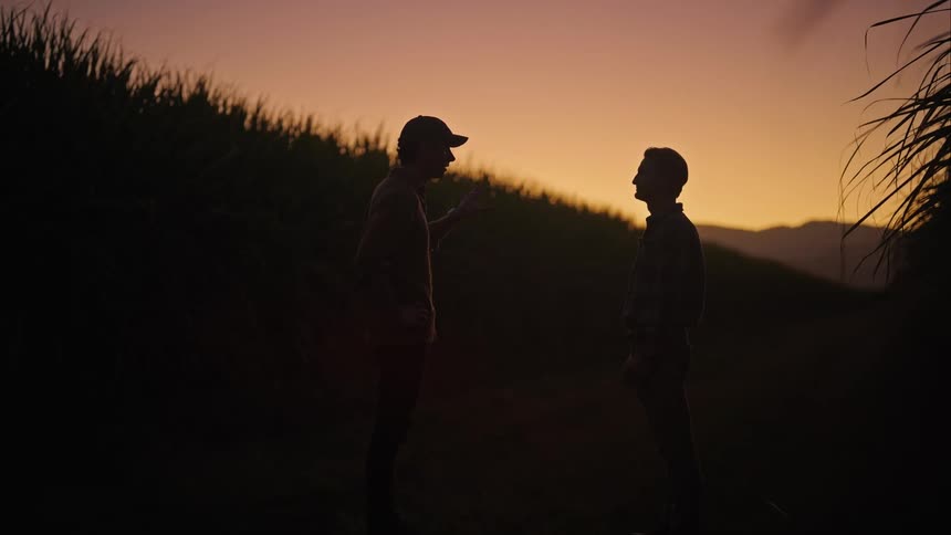 Two men are talking on a dirt road at sunset