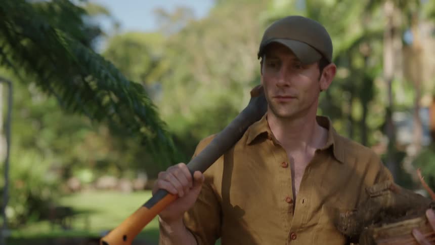 Man wearing cap holds toll and walks outdoors near trees
