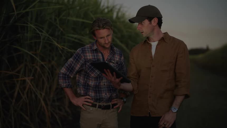 Two men conversing in a rural area with one of them holding a tablet and the other pointing in opposite directions