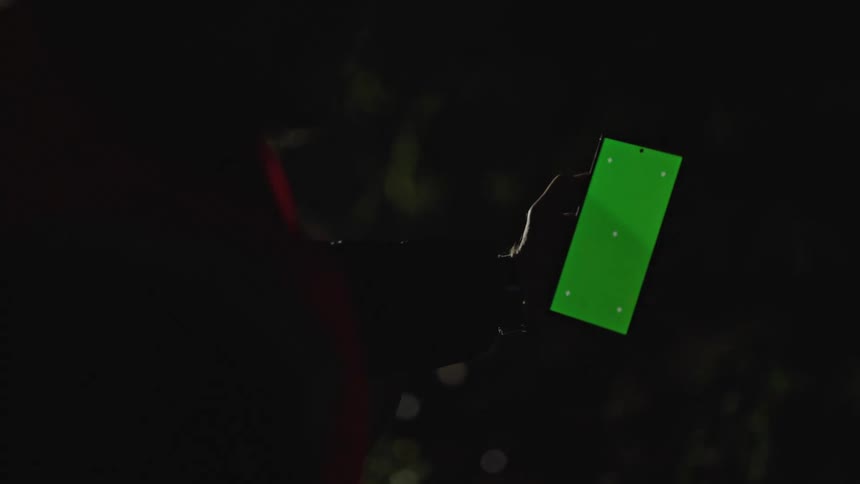 Worker looks at a smartphone with a green replaceable screen under flashing red lights at night