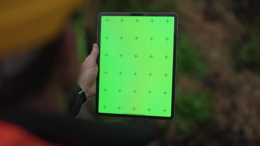 A man wearing safety clothing and a helmet running his hand over the tablet screen