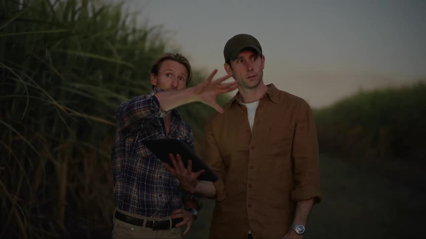 Two men standing in the bush using an ipad while talking to each other