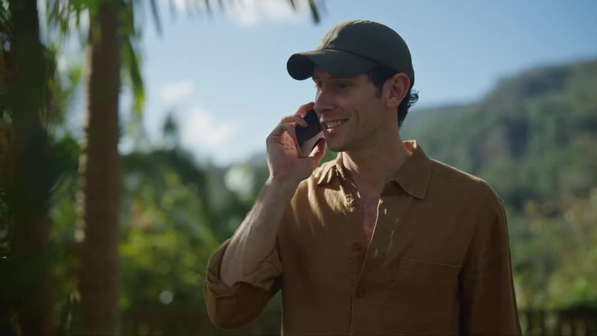 Man wearing a baseball hat answer the phone in the backyard