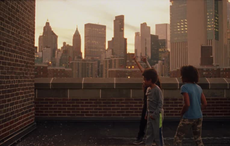 Three kids throwing objects at a brick wall and behind them is a view of the city