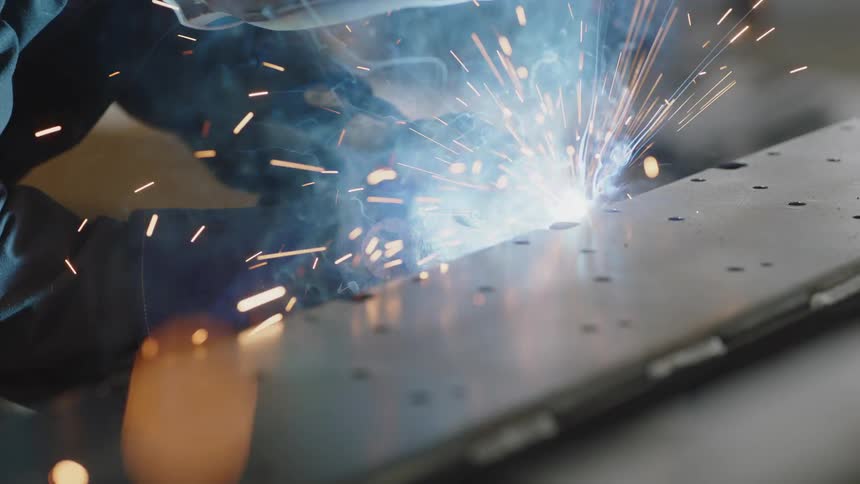 A person in protective gear welding iron parts
