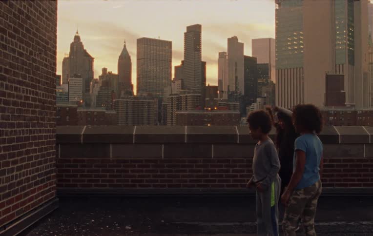Three children stand on a city rooftop and throw glass against a wall