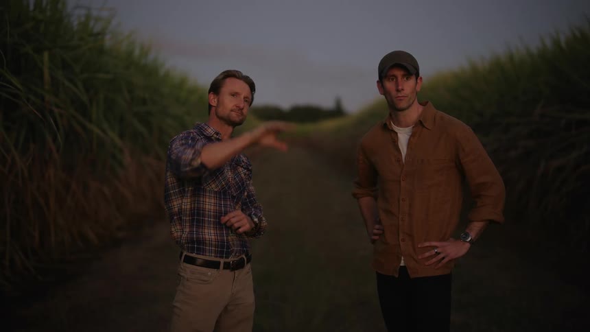 Two men talk and gesture standing next to fields of crops