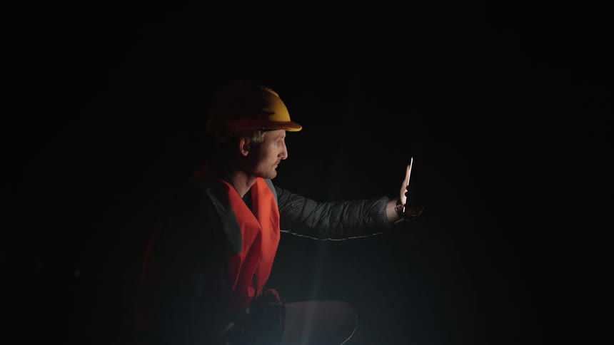 A man wearing a hard hat holds his cell phone on a dark night