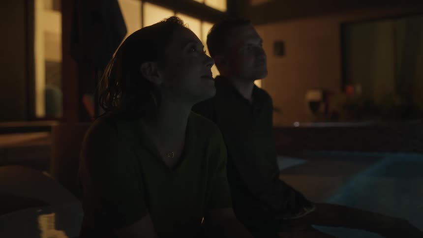 A soaked man and woman sitting in a swimming pool and thinking