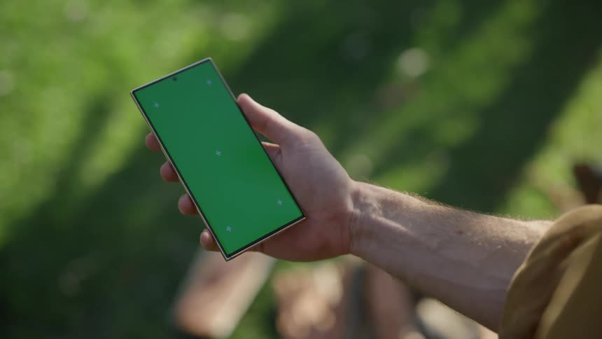 A mans hand holds up a smart phone to look at the screen