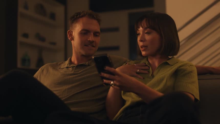 Man and woman sit on couch chatting as woman holds phone