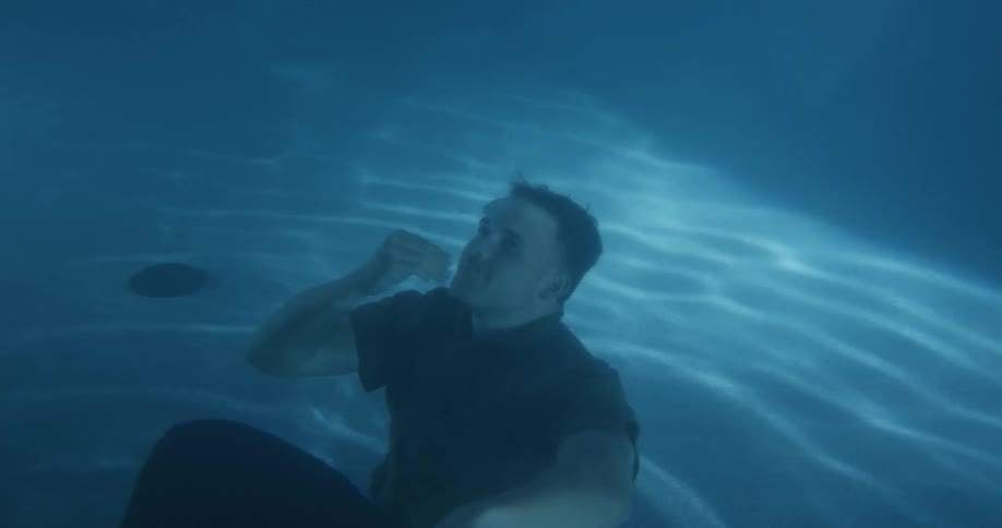 Fully clothed man submerges on a swimming pool at night