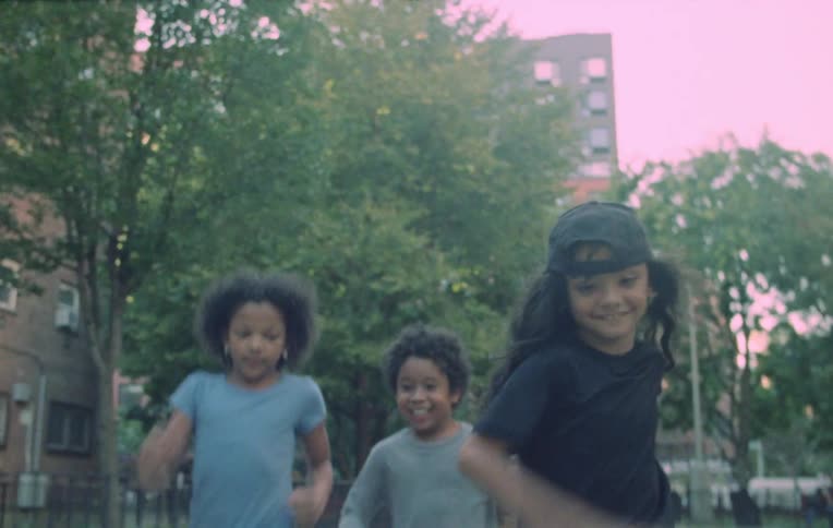 Three kids running on the side walk passing trees and buildings
