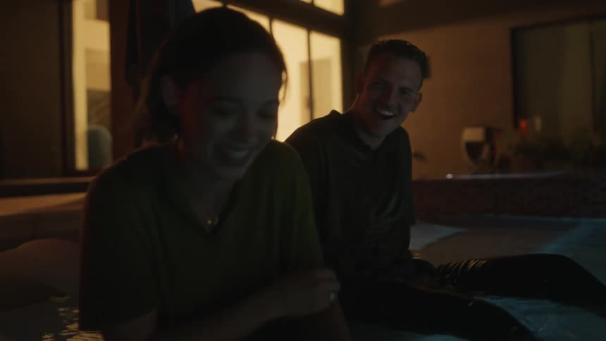 In a dimly lit room a man and a woman are joyfully immersed in a tub their laughter echoes through the air as they playfully interact