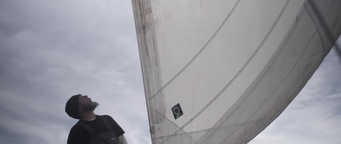 A man is pointing up and talking in front of a sail