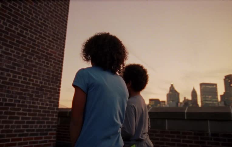 Three children throw toys at a wall on a rooftop in a city at sunset